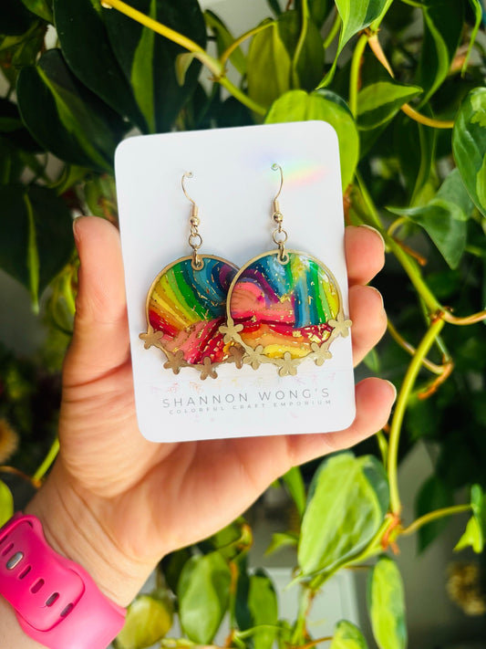 Rainbow bezel earrings held in hand for scale